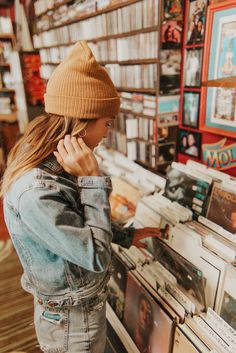 a woman is looking at records in a record store while talking on her phone and wearing a beanie