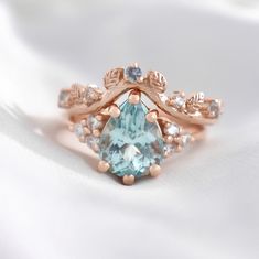 a ring with an aqua blue stone surrounded by white and rose gold leaves on it