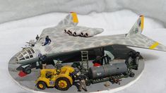 a model airplane with people around it on a snow covered ground next to a truck and tractor