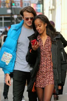 a young man and woman walking down the street looking at their cell phones while holding hands