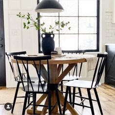 a dining room table with four chairs and a vase on top of it in front of a window