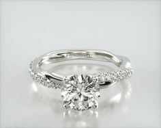 a white gold engagement ring with a round brilliant cut diamond in the center and pave set shoulders