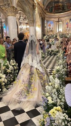 the bride is walking down the aisle in her wedding dress with flowers all over it