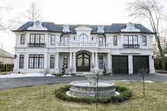 a large white house with a fountain in the front yard and two garages behind it