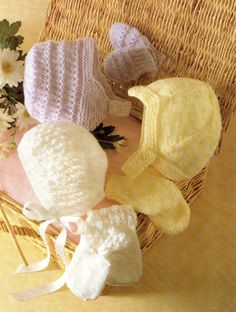 several knitted hats sitting on top of a wicker basket next to some flowers