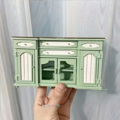 a hand holding up a miniature green cabinet