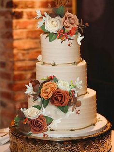 a three tiered cake with flowers and leaves on the top is sitting on a gold platter