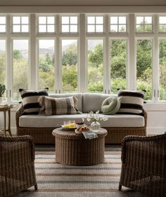 a living room with wicker furniture and large windows that overlook the trees in the distance