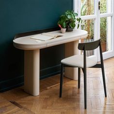 a white table with a plant on it in front of a window and a chair next to it