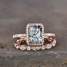 an engagement ring with a green and white stone surrounded by diamonds on top of a rock