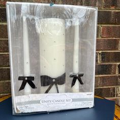 three candles with black bows on them in a clear box next to a brick wall