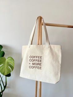 a canvas tote bag with coffee and more coffee printed on it hanging from a coat rack