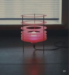 a pink lamp sitting on top of a wooden table next to a window with blinds