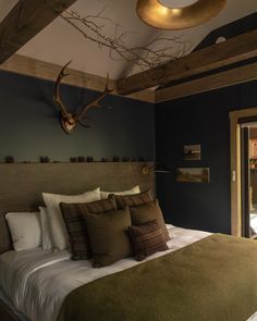 a large bed sitting under a wooden beam in a bedroom next to a doorway with a deer head on the wall