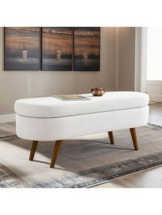 a white ottoman sitting on top of a rug in front of a wall mounted painting