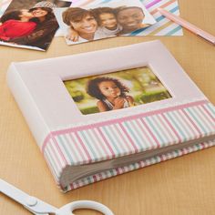 an open photo album sitting on top of a wooden table next to scissors and pictures