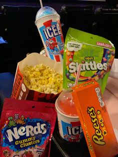 some snacks and drinks are sitting on a table with ice cream, chips, popcorn, and soda