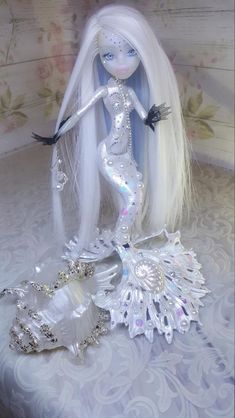 a doll with long white hair is sitting on a bed next to a sea shell