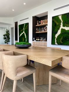 a large wooden table surrounded by chairs in a room with two paintings on the wall