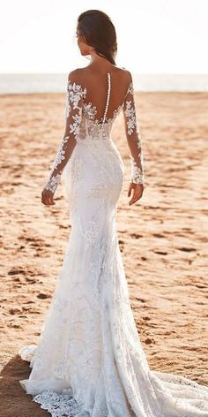 a woman standing on top of a sandy beach wearing a wedding dress with long sleeves