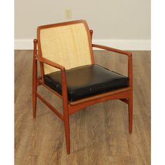 a wooden chair with black leather seat padding on wood flooring in front of a white wall