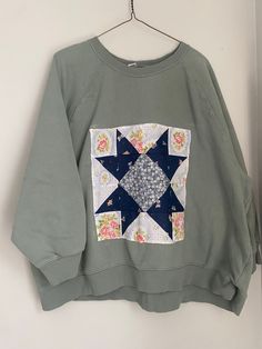 a green sweatshirt with a blue and white patchwork design on the front, hanging from a hanger