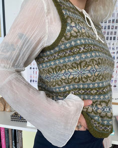 a woman is wearing a sweater and holding her hand on her hip while standing in front of a bookshelf