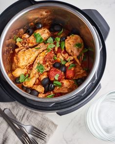 a pot filled with chicken and olives on top of a table next to a fork