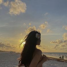 a woman standing on top of a sandy beach next to the ocean at sun set