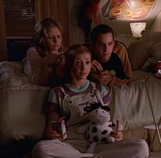 three people sitting on a couch with a stuffed animal in front of them and one person holding a drink