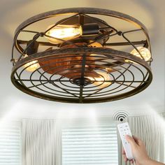 a person holding a remote control in front of a ceiling fan with light bulbs on it