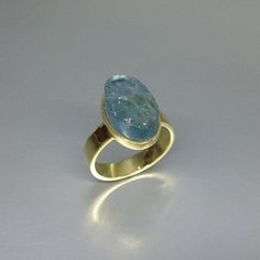 The sides of this raw stone ring are polished to secure a firm hold and give a the opportunity to cut a geometrical shape. It is set in 18K gold with a 4mm / 0.15inches band and a small rim embracing the stone. The stone is of high quality and stunns with its beautiful color. All our stones are natural stones and our jewelry is handmade, very slight differences may occur in color and size. Size stone: 14x8x8mm Aquamarine: The Romans believed it was sacred to Neptune and was a gift by the sirens, Fine Jewelry Aquamarine Oval Ring, Modern Aquamarine Oval Rings, Yellow Gold Aquamarine Rings For Gifts, Yellow Gold Aquamarine Ring As Gift, Modern Oval Aquamarine Rings, Modern Oval Blue Topaz Ring, Oval Aquamarine Wedding Ring, Luxury Blue Oval Moonstone Ring, Oval Aquamarine Birthstone Ring For Anniversary