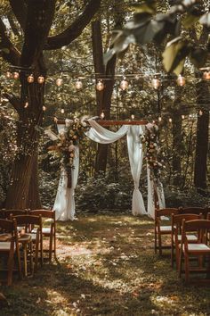 an outdoor wedding setup with white draping and lights hanging from the tree branches