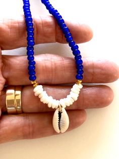 Beaded shell choker with cobalt blue African glass beads, Hawaiian white puka shells, genuine cowrie shell and Karen Hill Tribe 24k gold vermeil accents. Beaded summery necklace features vintage cobalt blue African white heart trade beads and genuine sea shells. Little white Hawaiian puka shells and genuine cowrie shell focal. Karen Hill Tribe 24k gold vermeil cube beads add fabulous accents. Beaded necklace closes with 14k gold fill spring ring clasp and findings. Blue Beaded Shell Necklace Ocean-inspired, Ocean-inspired Blue Beaded Shell Necklace, Vacation Shell Jewelry In Blue, Blue Shell-shaped Jewelry For Vacation, Blue Shell Jewelry With Colorful Beads, Blue Shell Necklace With Colorful Beads For Beach, Blue Shell Necklace With Colorful Beads For Vacation, Blue Strand Shell Necklace For Vacation, Blue Beaded Shell Necklace For Beach