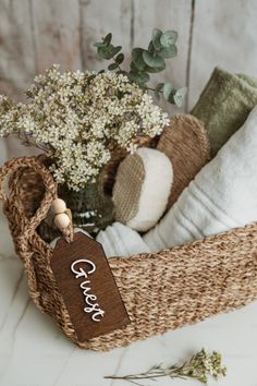 a basket filled with white flowers and personalized items next to a bottle of wine