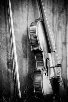 a black and white photo of a violin leaning against a wooden wall with the strings still attached