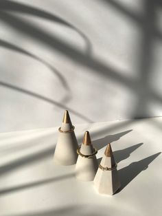 three white vases sitting on top of a white table next to a shadow cast wall