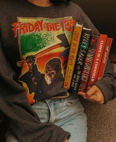 a woman sitting on a couch holding several books in her hands and wearing a shirt with the words friday the 13th printed on it