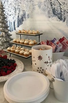 a table topped with plates and cups filled with desserts next to a snow covered forest