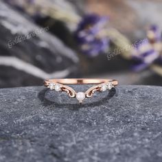 a rose gold ring with white diamonds on top of a stone slab in front of purple flowers