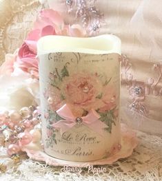 a candle that is sitting on a lace doily with pink flowers and pearls around it