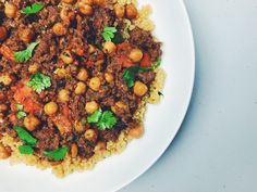 a white plate topped with rice and meat covered in garbanzo beans, parsley