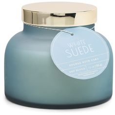 a white candle with a blue label on the lid that says, white suede