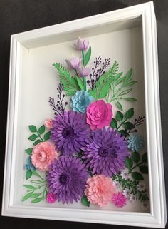 paper flowers in a white frame on a table