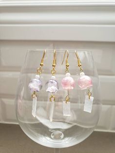 five different colored glass beads hanging from gold earwires on a clear wine glass