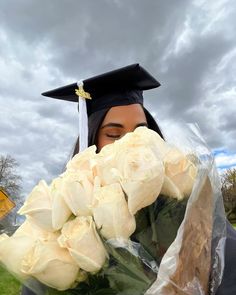 a woman wearing a graduation cap and gown holding flowers in front of her face while looking at the camera