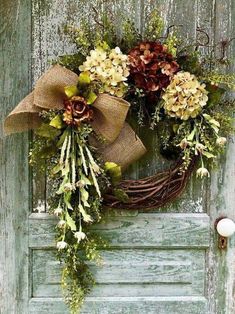 a wreath is hanging on the front door with pine cones and other flowers in it