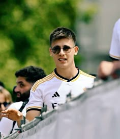 a young man wearing sunglasses standing in front of a soccer ball net with his hand out