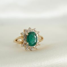 an oval emerald and diamond ring on a white cloth with the background in soft focus