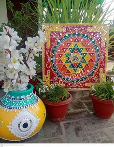 two vases with plants and flowers in them on the ground next to a painting